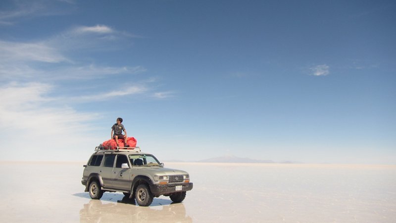A male student poses on top of an off-road vehicle on a beach in America