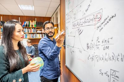 Research Fellow Maggie Lieu and Post doc Swagat Mishra at a white board, discussing the expansion of the Universe, and the evidence for the Big Bang i.e. the Cosmic Microwave Background (the inflatable ball) in Cripps North Building