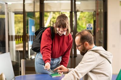 Student showing phone to Library Adviser at front desk Hallward Library