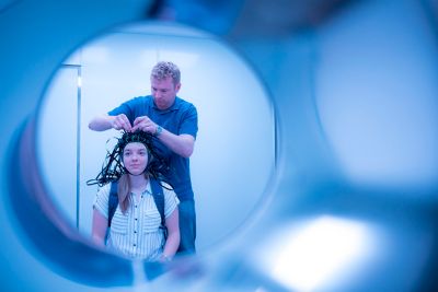 Professor attaching MEG system that can be worn like a helmet, allowing free and natural movement during scanning, to a female PhD student October 2019. Photography by Lisa Gilligan-Lee.Copyright belongs to the University of Nottingham.https://www.nottingham.ac.uk/research/beacons-of-excellence/precision-imaging/our-projects/meg/meg.aspx