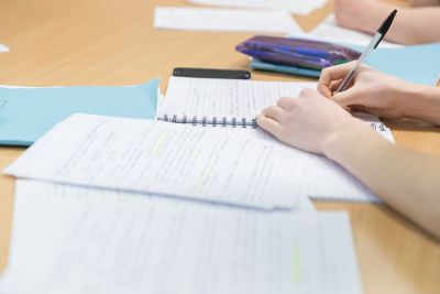 Close up of student's hand and arm writing notes in maths undergraduate workroom