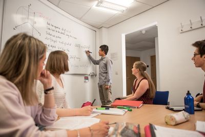Student writing maths problems out on paper take from over shoulder with laptop on desk in front