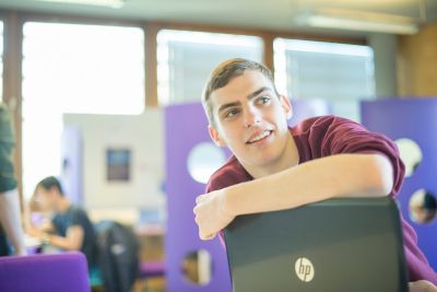 Undergraduate smiling student arm rested on laptop screen in robotics lab
