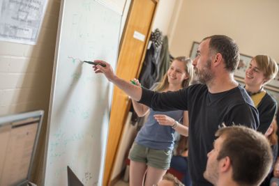Professor Phillip Moriarty writing on a whiteboard, surrounded by smiling students