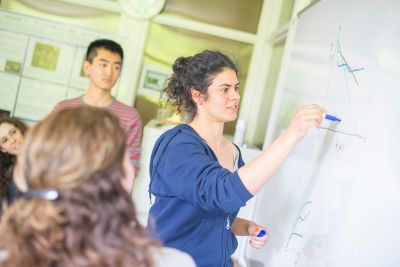 Physics student drawing a graph on a whiteboard with staff member and undergraduate students looking on