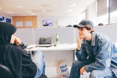 Undergraduate students at a computer desk talking in the Product Design Studio