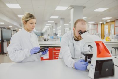 Undergraduate student with glasses, wearing gloves and holding up a petri dish sample