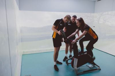 Undergraduate students watching someone on a Wattbike in the Immersive Suite