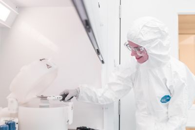 Undergraduate student wearing protective clothing and smiling whilst using equipment in the nanoscience lab