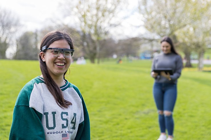 Two undergraduate psychology students in a grassy park. One of them is wearing experimental eyeglasses