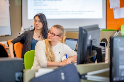 EPSRC Horizon CDT PhD students in module discussion group - one student in cream jumper with glasses making notes, with a second student behind in a dark grey blazer and blue t-shirt