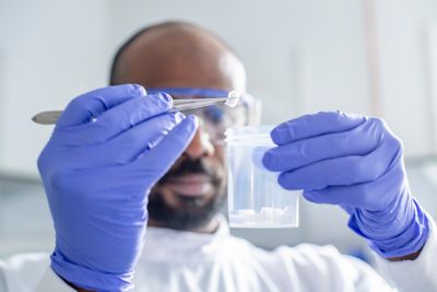 Postgraduate research student with a sample of 3D printed PCL held above a cylindrical tub by tweezers
