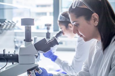 Postgraduate research students looking at a sample of printed parts through a microscope