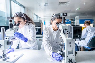 Postgraduate research students looking at a sample of printed parts through a microscope