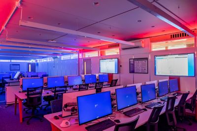 Cyber security lab full of desks with computer and monitors switched on, room lit red and blue