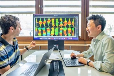 Associate Professors Robert Laramee and Kai Xu reviewing data on their laptops with an image of four angular histograms on a monitor behind them