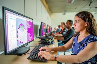 Assistant Professor Ayse Kucukyilmaz in computer room sat working at a screen with other staff/students at the desks in the room