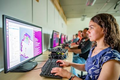 Assistant Professor in computer room sat working at a screen with other staff/students at the desks in the room