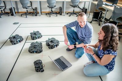 Simon Castle-Green Technical Manager and Assistant Professor Ayse Kucukyilmaz in Robot lab sat on the floor directing robots with a laptop