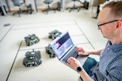 Technical Manager in Robot lab sat on the floor directing robots with a laptop