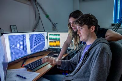 Researchers Filipe Louly Quinan Junqueira and Connor Fields looking inside an ultra-high vacuum (UHV) scanning probe microscope (SPM) chamber