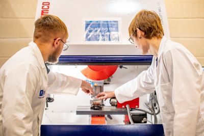 Undergraduate students placing a pre-prepared aluminum billet into the Computer Numerical Controlled (CNC) milling machine