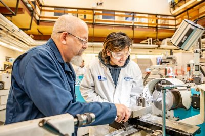Technician works with student on a centre lathe turning metal