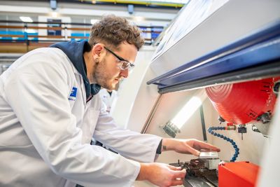 Undergraduate student placing a pre-prepared aluminum billet into the Computer Numerical Controlled (CNC) milling machine