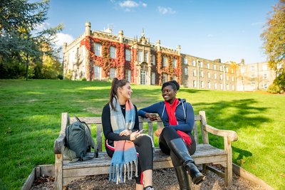 Two students chatting on bench outside in sunshine