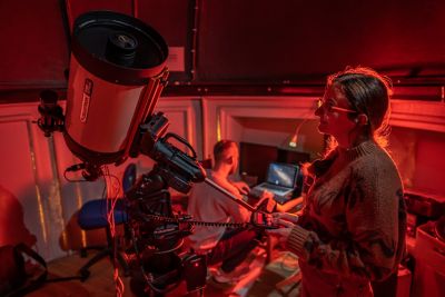 Postgraduates Kelly de Vos and Bradley March operating the telescope in a telescope dome lit up red