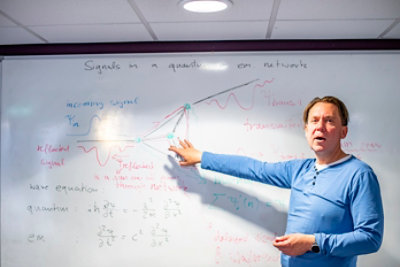 Associate Professor Dr Sven Gnutzmann explaining the information on lecture white board titled 'signals in a quantum or em. network'